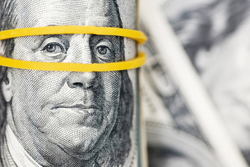 A roll of 100 dollar bills close-up on a pile of American dollars. Background from banknotes of 100...