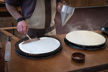 Baker's hands pouring sweet on the griddle for the sweet crepe's preparations.