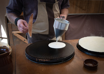 Baker's hands pouring sweet on the griddle for the sweet crepe's preparations.