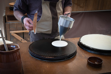 Baker's hands pouring sweet on the griddle for the sweet crepe's preparations.