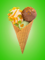 Pistachio, chocolate and vanilla ice cream balls with caramel sauce and nuts in waffle cone on a color background