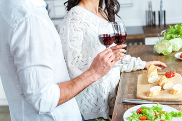 cropped view of couple clinking glasses of red wine near table with bread and salad