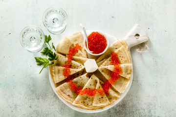 Traditional Russian pancakes with red caviar and butter on the table and two glasses of vodka