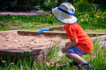 A boy with a bucket and a shovel playing in the sand. Children's games. Summer and sand. The boy has a bright photo. The boy plays
