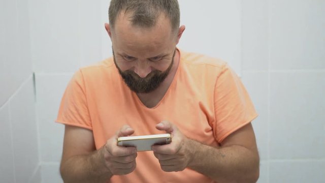 close-up of a man who plays phone while sitting on the toilet