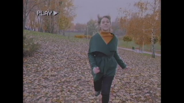 Young woman walks in the autumn park. Cheerful woman with blond hair in a green coat walks on the yellow leaves. Girl with a bouquet of leaves in her hands. Old video. Home video archive. Family video