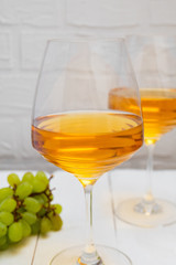 Glasses of Amber wine or scin-fermented white wine with grapes on white wooden background.
