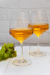 Glasses of Amber wine or orange wine with grapes on white wooden background.