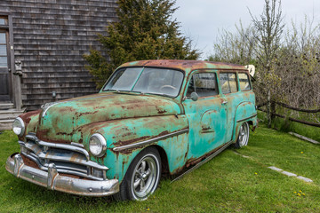 surf board hangs out the back of an old rusting neon green car