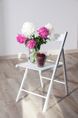 bouquet of red peonies in a vase stands on a white chair in the interior