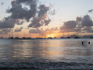 Sailboats in tropical laggon with the sunsetting behind the clouds and masts