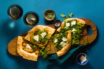 traditional Italian white pizza with taleggio and pecorino cheese, caramelized pumpkin and arugula on the blue table