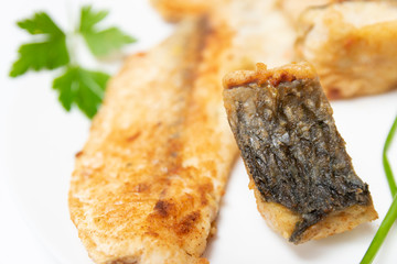 Tasty food, nutrition, kitchen and culinary concept: closeup pieces of fried, baked, golden and tasty fish on a white plate.