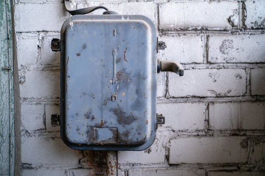 Metal electrical fuse box attached to white brick wall
