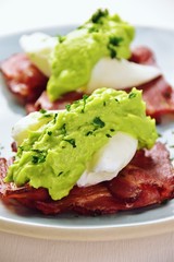 Paleo eggs benedict with avocado sauce on a bacon mat 