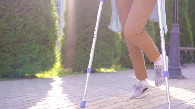 unrecognizable disabled woman with an injury on crutches walking in the Park Sunny