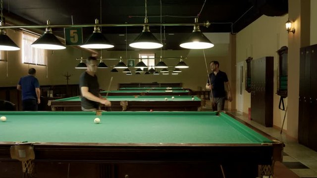 Men playing billiards, hitting the balls with a cue into pockets on a billiard table. 4K