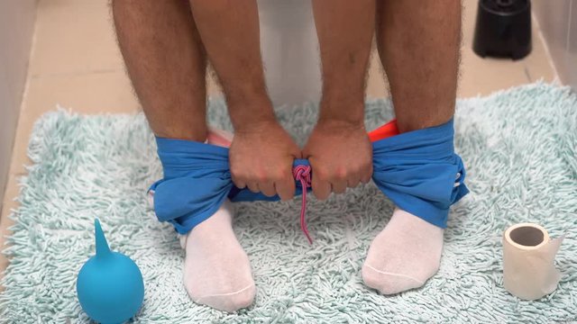 legs of a man sitting on the toilet with blue shorts lowered