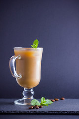 Iced coffee with milk on a dark background. Latte and fresh mint on a slate board. Summer drink in a glass, and coffee beans. Copy space