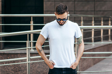 A young stylish man with a beard in a white T-shirt and glasses. Street photo