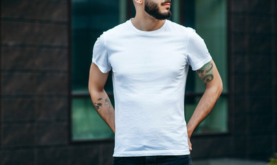 A young stylish man with a beard in a white T-shirt and glasses. Street photo - obrazy, fototapety, plakaty