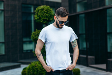 A young stylish man with a beard in a white T-shirt and glasses. Street photo