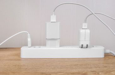 Many electrical plugs connected to a power white strip or extension block on wooden table. High-tech smart strip