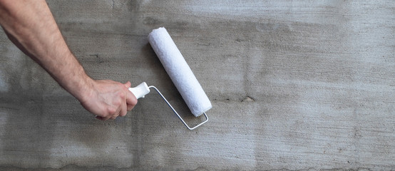 Priming the wall with a paint roller. Builder's hand with paint roller close-up. Panoramic photo....