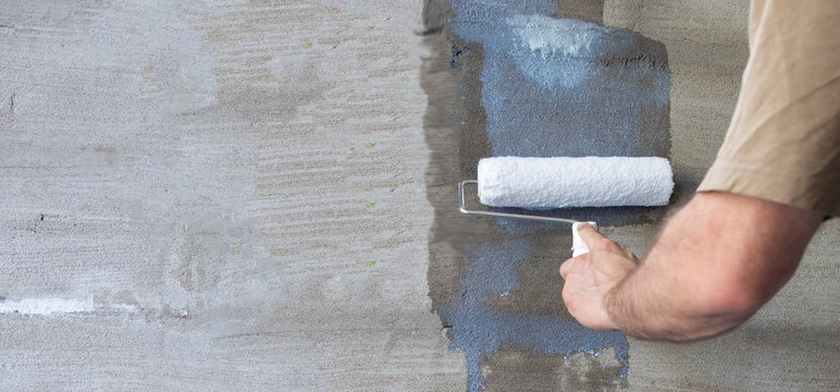 Priming the wall with a paint roller. Builder's hand with paint roller close-up. Panoramic photo. Copy space