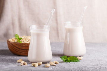 Organic non dairy cashew milk in glass and wooden plate with cashew nuts on a gray concrete background.