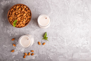 Organic non dairy almond milk in glass and wooden plate with almond nuts on a gray concrete background.