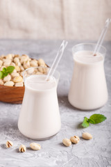 Organic non dairy pistachio milk in glass and wooden plate with pistachio nuts on a gray concrete background.