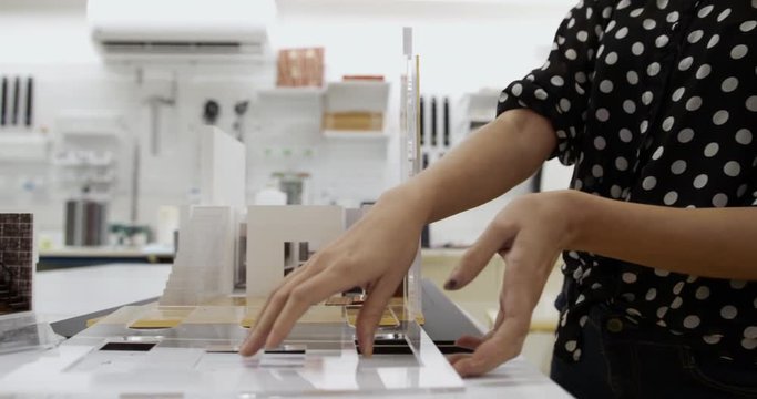 People at work in architecture design studio with plastic model and mock-up of new building. Busy young woman working as artist in laboratory. Girl and professional occupation