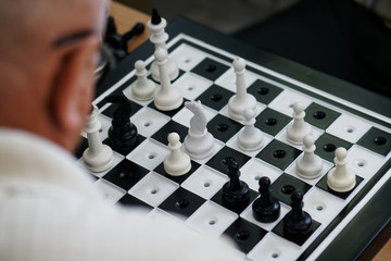 An elderly man with glasses plays special chess for the blind