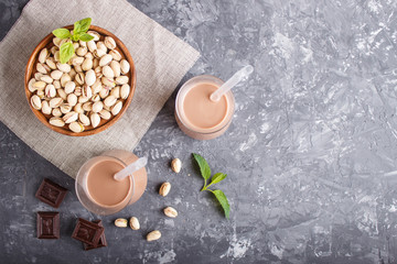 Organic non dairy pistachio milk in glass and wooden plate with pistachionuts on a black concrete background.