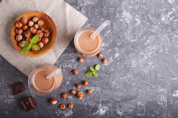 Organic non dairy hazelnut chocolate milk in glass and wooden plate with hazelnuts on a gray concrete background.
