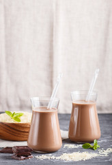 Organic non dairy rice chocolate milk in glass and wooden plate with rice seeds on a black concrete background.