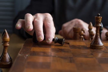 Fototapeta na wymiar The hand of an old man puts a black king's figure on the board acknowledging loss, concept business games, selective focus