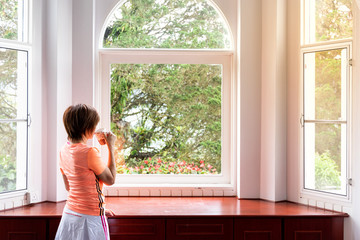 Woman admiring natural scenic sunrise from home interior with coffee