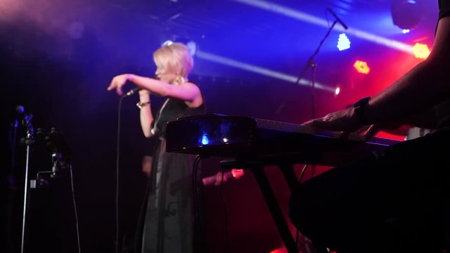 Female singer performs on the stage on the background. Keyboardist on the foreground. Slow motion