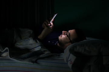 Man looking his mobile phone in the bed at night