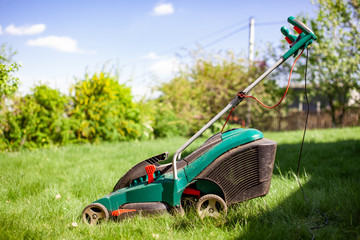 Close up of  lawn mower on green grass. Worker doing his job in backyard. Spending summer day in garden. Nobody..