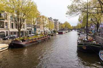 Fototapeta na wymiar AMSTERDAM, NETHERLANDS - APRIL 13, 2019: Houses and Boats on Amsterdam Canal
