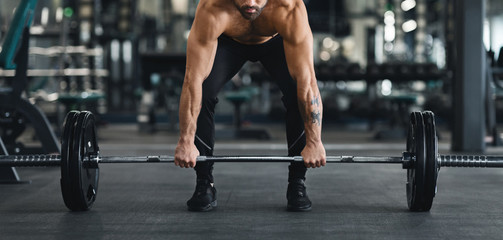 Muscular guy lifting heavy barbell from gym floor