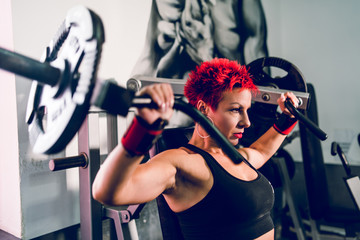 Fototapeta premium Young muscular woman female athlete bodybuilding at the gym training shoulder press machine fitness weight loss