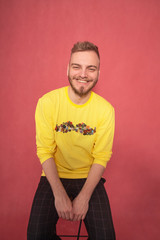 one young grinning man sitting on a bar stool, while looking into camera.