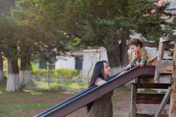 Side view of mom looking at her little son on the slide in the park outdoors