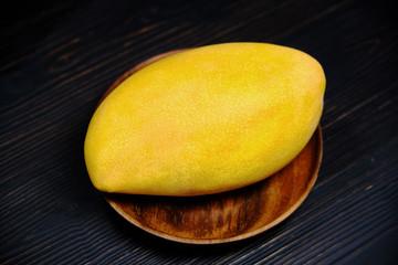 Yellow mango on a dark wood background. Tropical fruit on a wooden saucer, close-up. Big mango on the kitchen table.