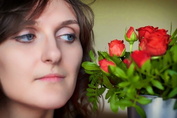 A young woman looks at a bouquet of red roses, close-up. Portrait of a girl with a bouquet of flowers near her face.