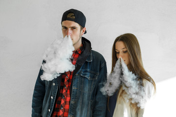 Vape teenager. Young cute girl in casual clothes and handsome guy in a cap smoke an electronic cigarette outdoors. Bad habit that is harmful to health. Vaping activity.